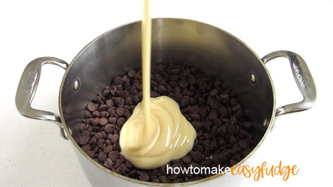 sweetened condensed milk being poured into a pan of chocolate chips to make chocolate fudge
