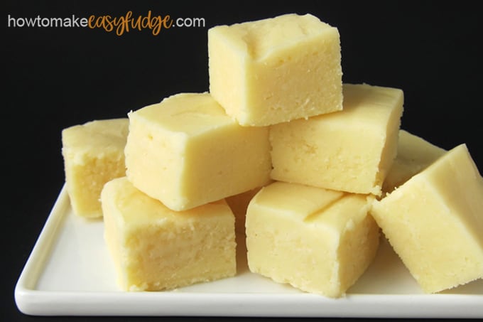 Squares of homemade lemon fudge stacked up on a white plate on a black background