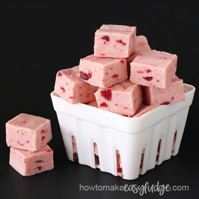 square of strawberry fudge stacked in a strawberry container on a black background