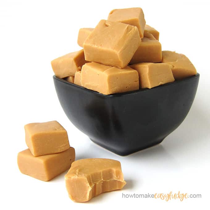 Small black bowl filled with squares of homemade butterscotch fudge with a few pieces set in front of the bowl. 