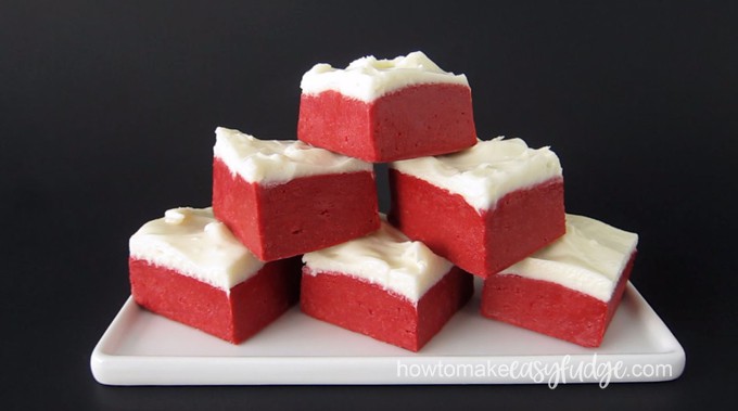 six squares of red velvet fudge stacked on a white rectangle plate set on a black background