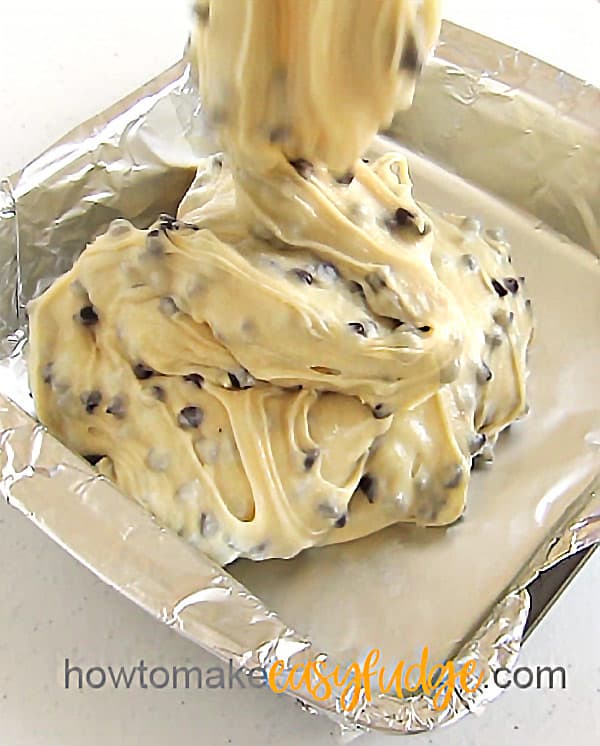 cookie dough fudge being poured into a tin foil lined 8-inch square pan