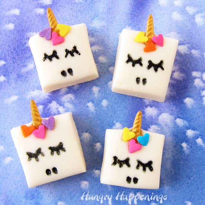 4 squares of white chocolate Fudge Unicorns on a blue watercolor background