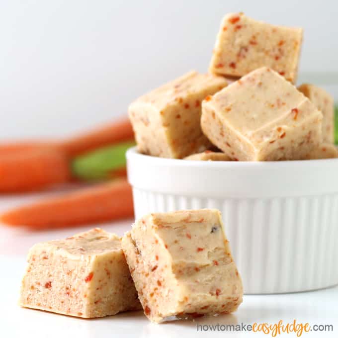pieces of 2-ingredient, microwave, carrot cake fudge piled up in a white ramekin set in front of fresh carrots
