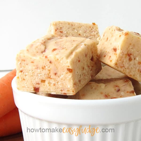 squares of homemade carrot cake fudge in a white ramekin sitting in front of a few carrots