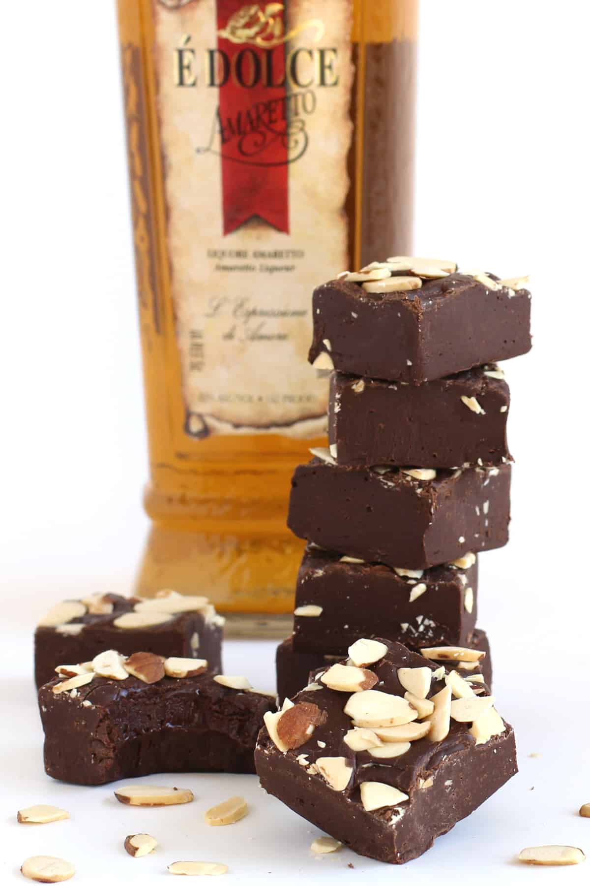 Chocolate Amaretto Fudge topped with sliced almonds stacked in front of a bottle of Amaretto