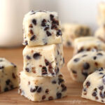 Chocolate chip cookie dough fudge stacked up in front of a glass of milk