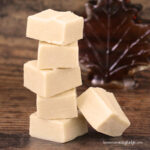 maple fudge squares stacked in front of a leaf-shaped maple syrup bottle