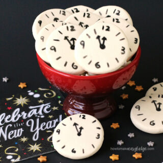 New Year's Eve fudge clocks in a red bowl set next to a New Year's napkin and gold and silver stars