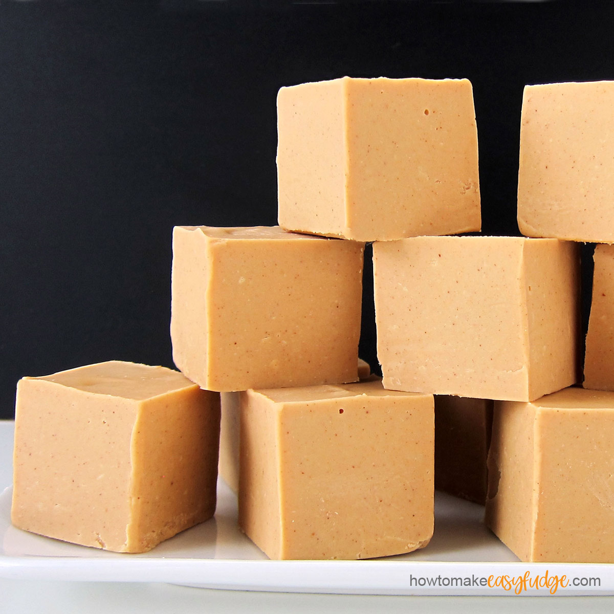 thick squares of creamy peanut butter fudge stacked on a white plate on a black background