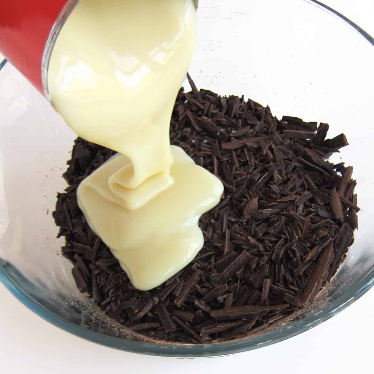 pouring sweetened condensed milk into a bowl of finely chopped chocolate