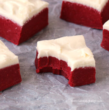 red velvet fudge topped with a layer of cream cheese frosting sitting on crinkled parchment paper