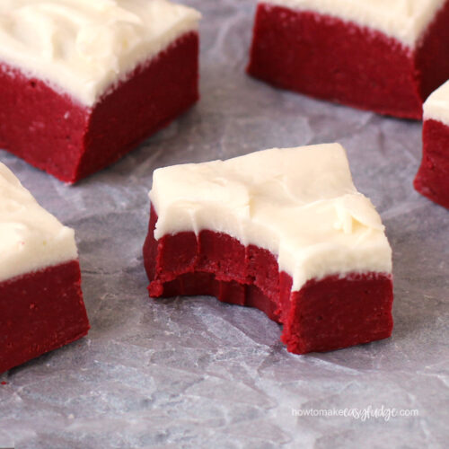 red velvet fudge topped with a layer of cream cheese frosting sitting on crinkled parchment paper