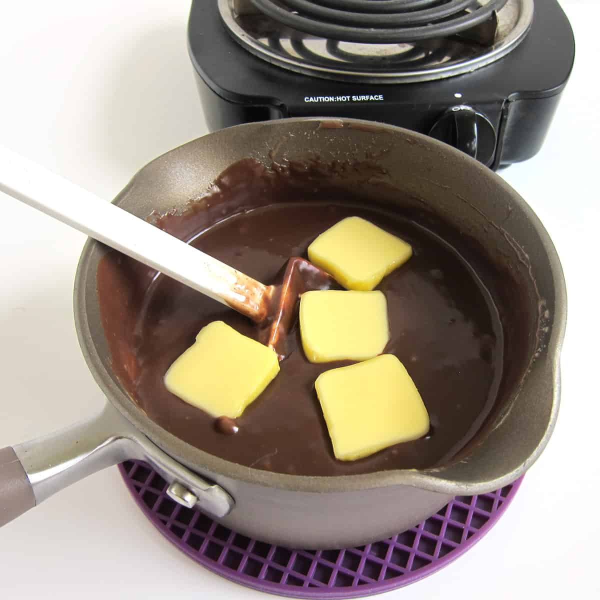 Adding 2 tablespoons of butter to the hot fudge sauce in the saucepan off heat.