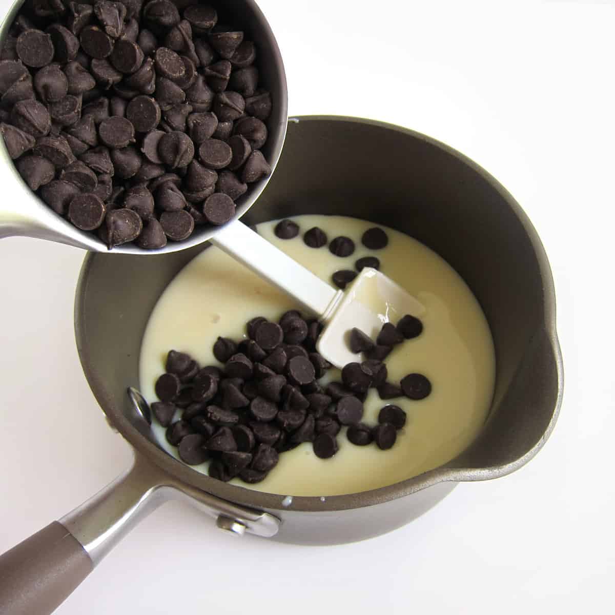 Pouring chocolate chips into a saucepan filled with sweetened condensed milk.