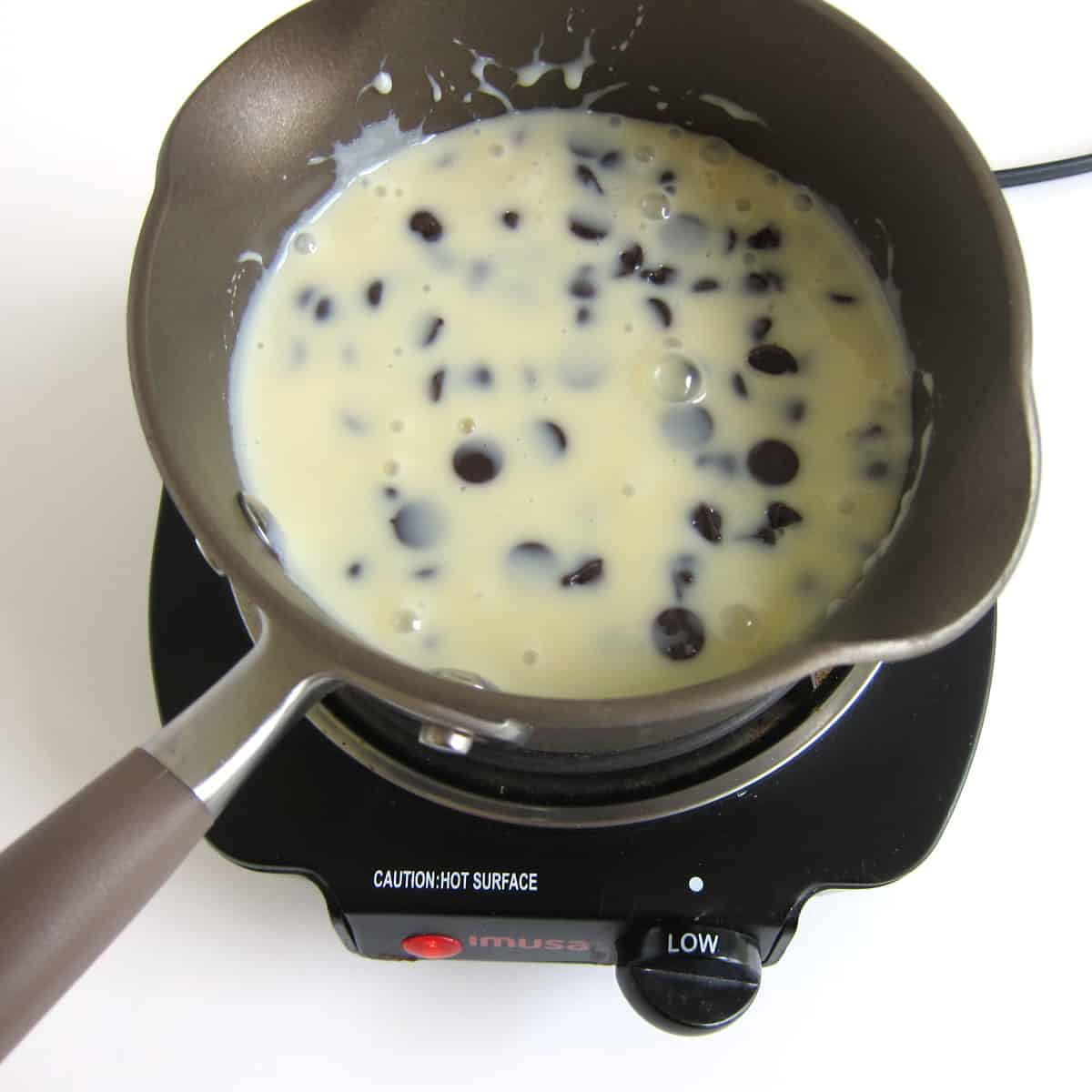Chocolate chips and sweetened condensed milk melting over low heat in a saucepan.
