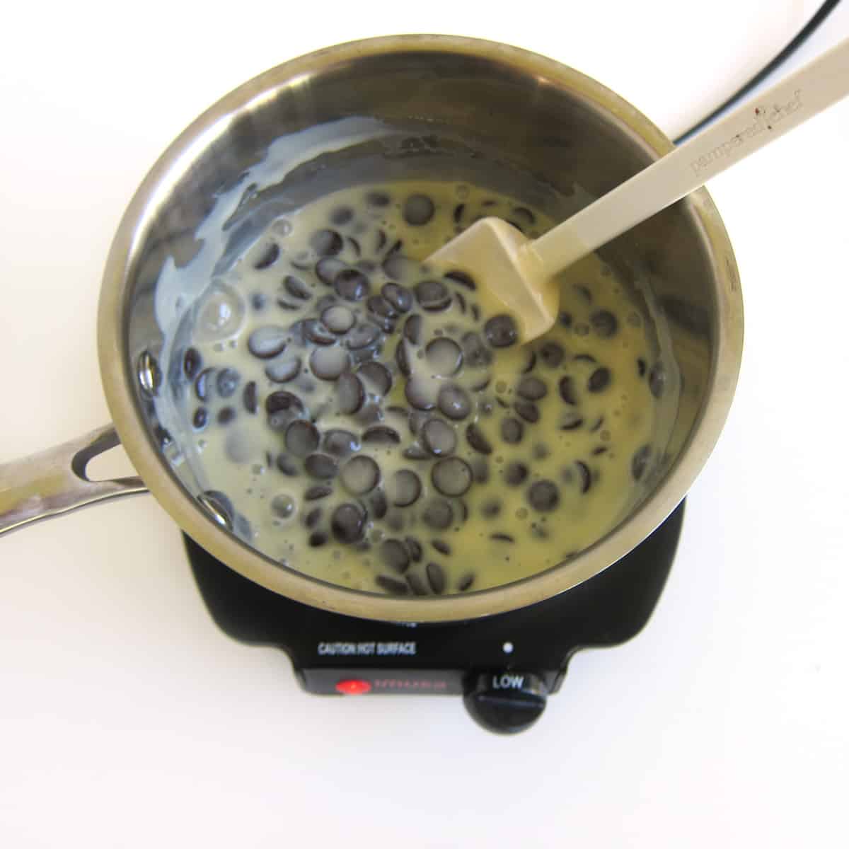 chocolate chips and sweetened condensed milk stirred together in a saucepan set over low heat