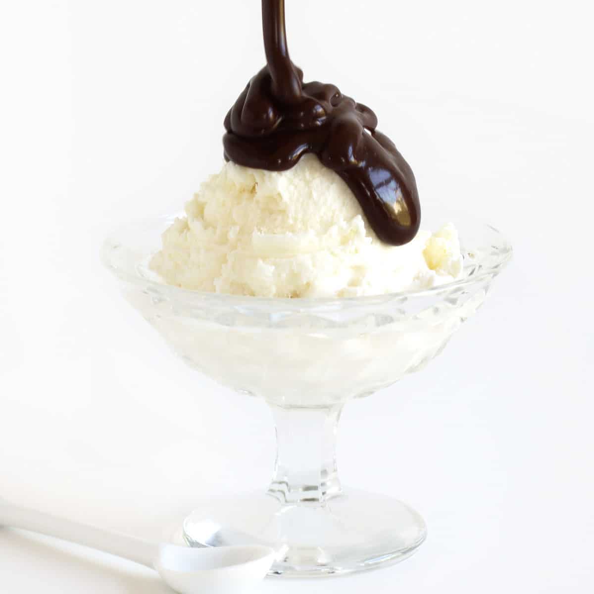 Pouring hot fudge sauce over a scoop of vanilla ice cream in a glass bowl.