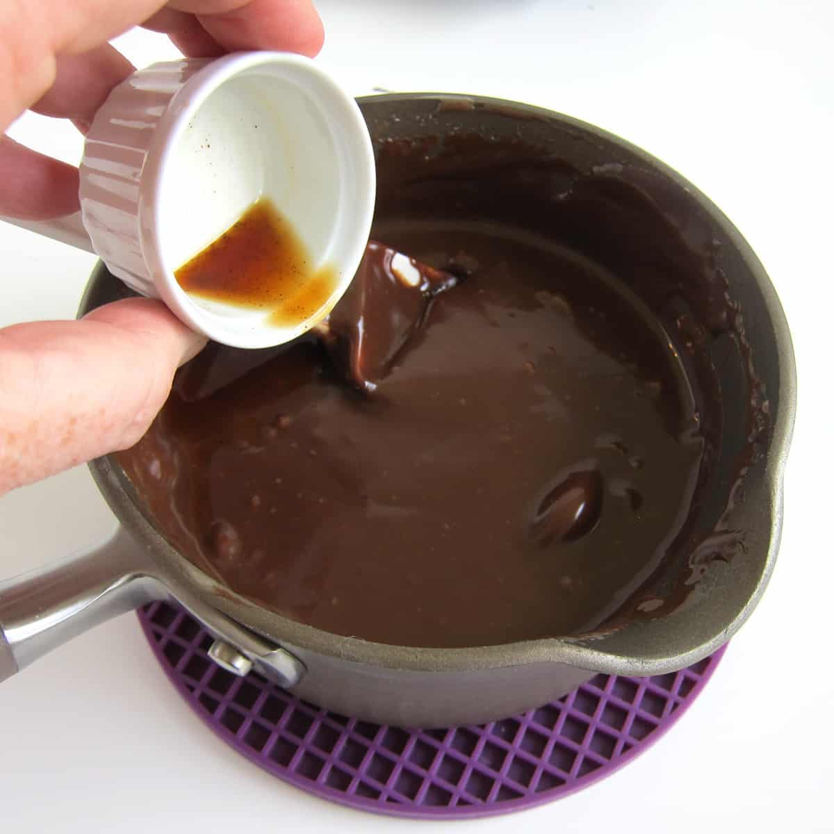 Pouring vanilla extract into a saucepan filled with hot fudge sauce.