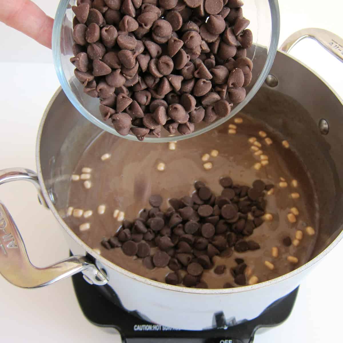 pouring milk chocolate chips into the hot chocolate and sweetened condensed milk blend.