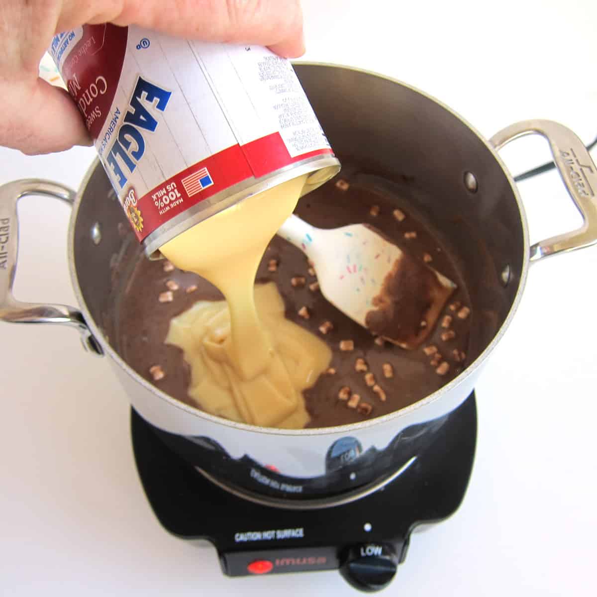 pouring sweetened condensed milk into a pan of hot cocoa.