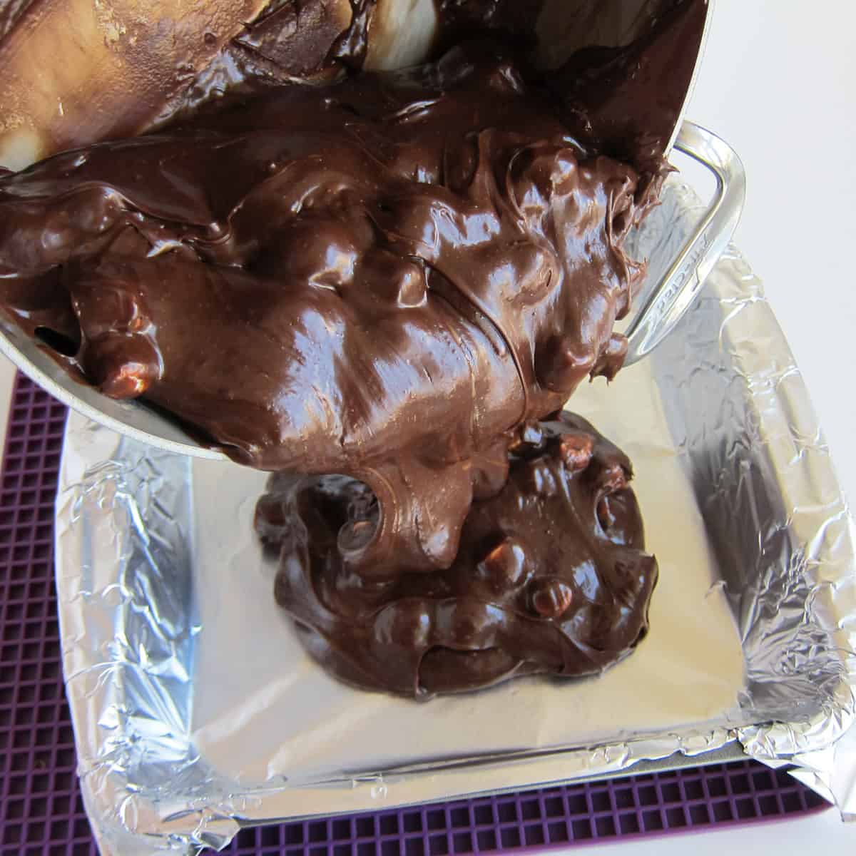 pouring hot chocolate fudge into a square baking pan that's lined with non-stick tin foil.