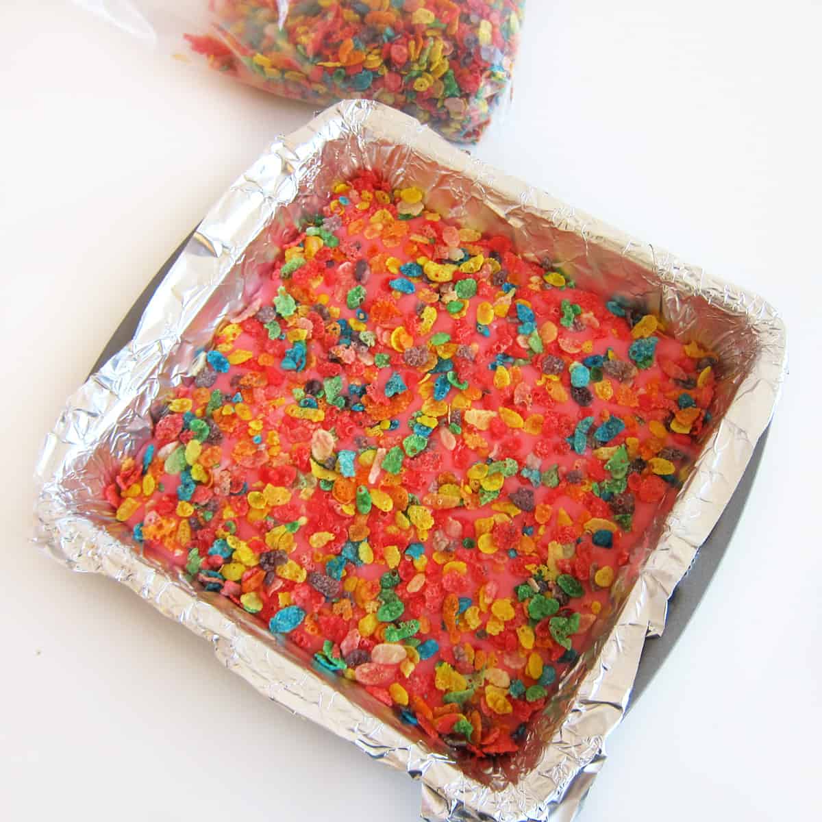 tin foil-lined square baking pan filled with pink Fruit Pebbles Fudge.